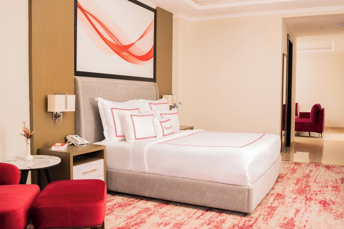 A hotel room with a bed, a desk, a chair, and a reception area.