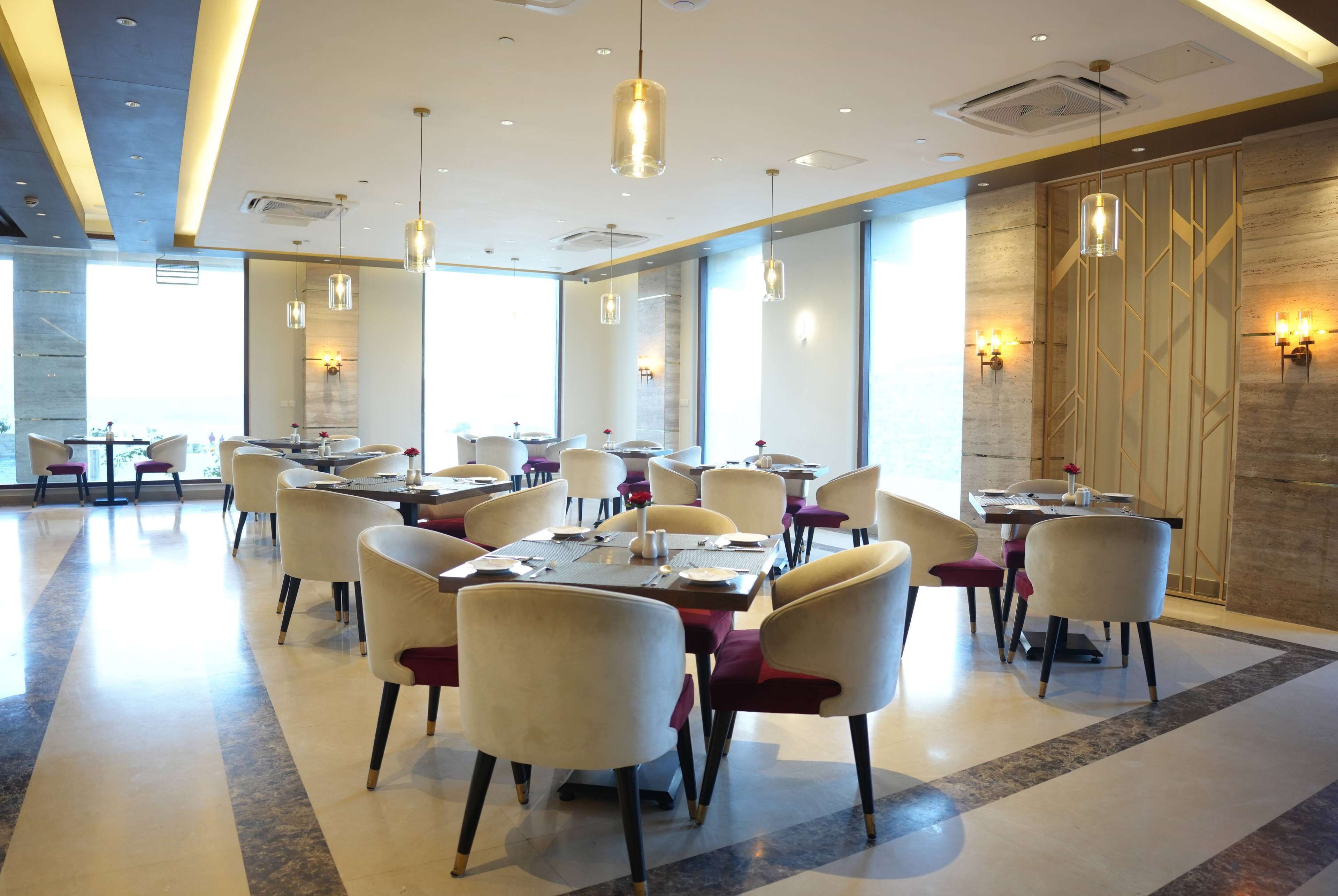 A modern dining area with tables and chairs, large windows, and decorative wall lighting.