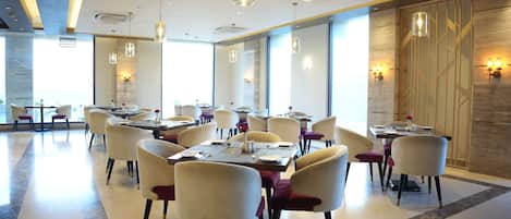 A modern dining area with tables and chairs, large windows, and decorative wall lighting.