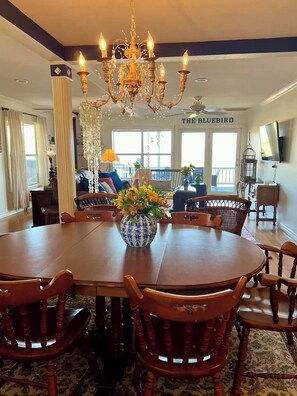 Un comedor con una mesa redonda, sillas de madera, una araña y un jarrón con flores.