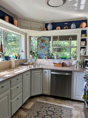 Una cocina con armarios blancos, lavavajillas, un lavamanos y una ventana con diseño de vitral.
