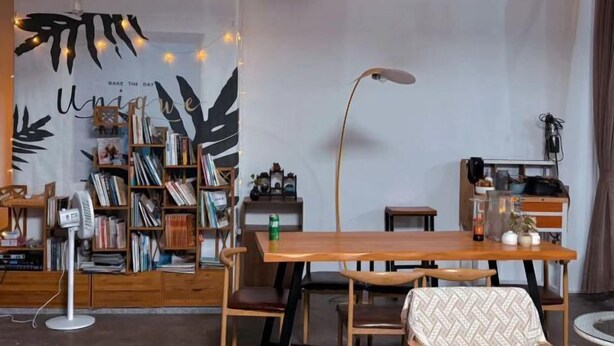 A cozy room with a wooden table, chairs, a bookshelf, and a wall with a leaf pattern and motivational quote. - Yueting Nanshe Homestay (Renhua)