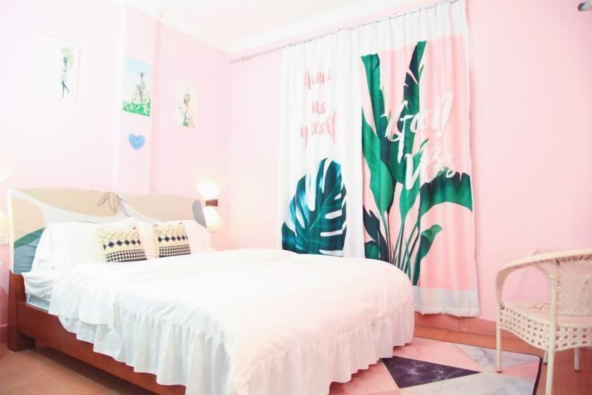A bedroom with a bed, a chair, and a curtain with a tropical leaf pattern.