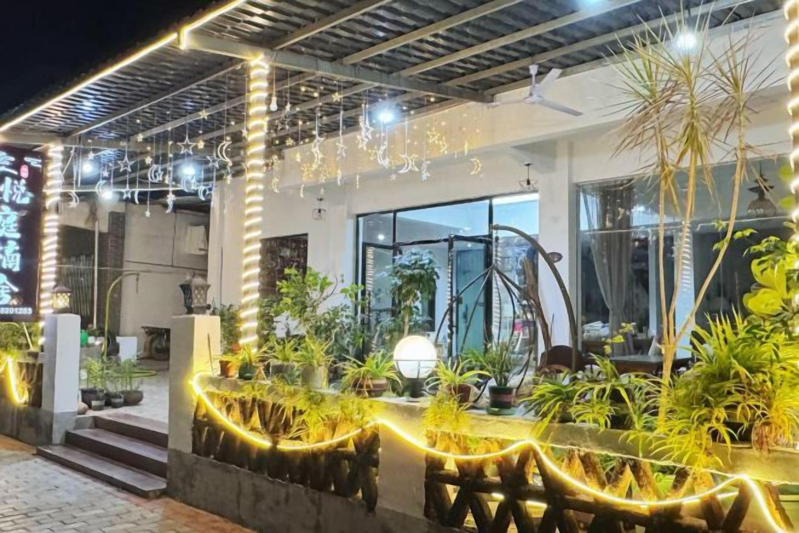 A hotel entrance with a covered outdoor area, potted plants, and a well-lit pathway.