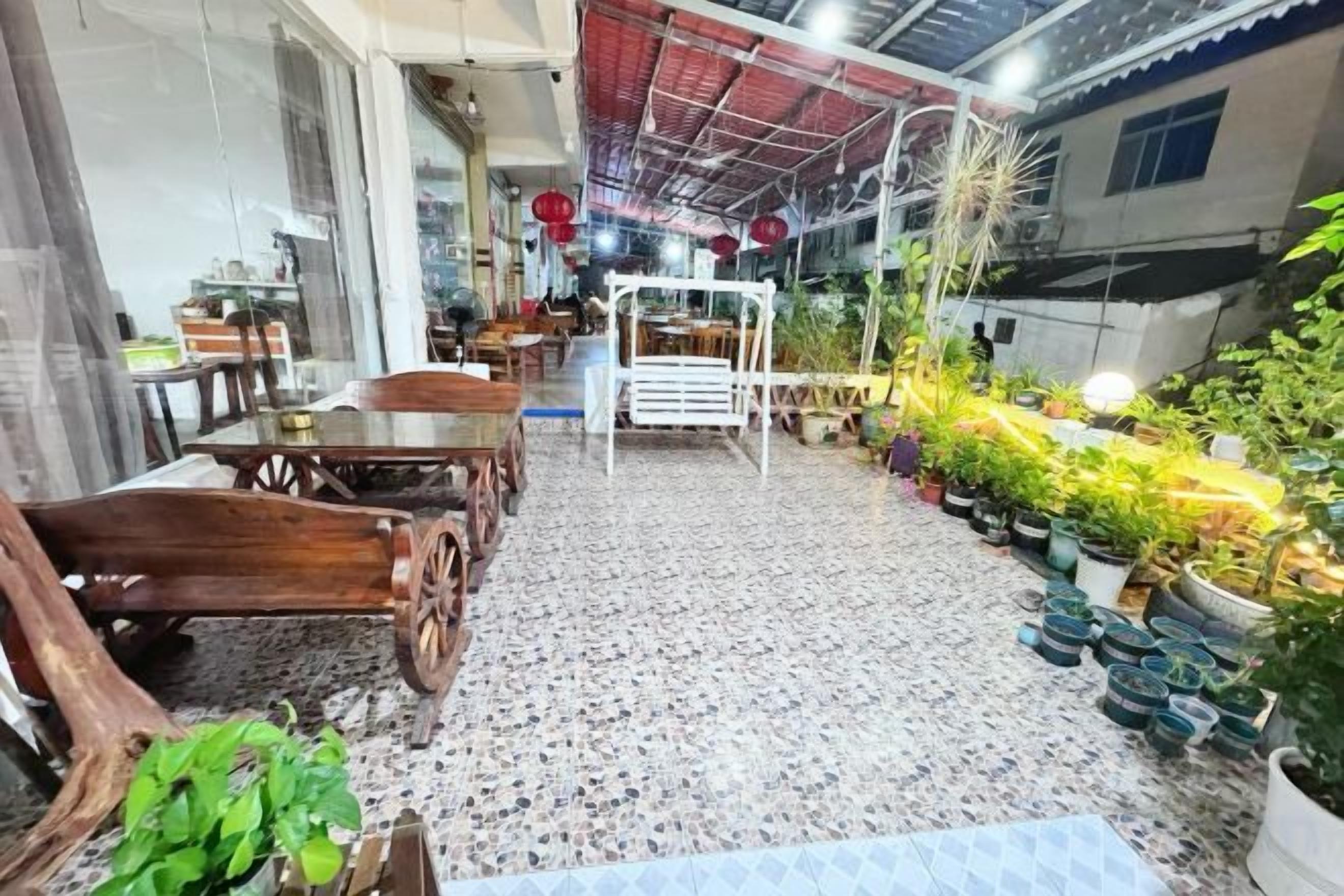 A covered patio area with a dining table and chairs, surrounded by potted plants and a variety of greenery.