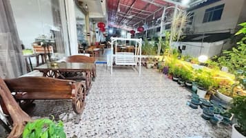 A covered patio area with a dining table and chairs, surrounded by potted plants and a variety of greenery.