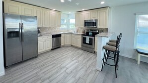 A modern kitchen with light wood cabinets, stainless steel appliances, and a bar area with stools. - Waterfront Retreat 4 BR, 3 BA screened & heated pool, gorgeous canal views (Rotonda West)