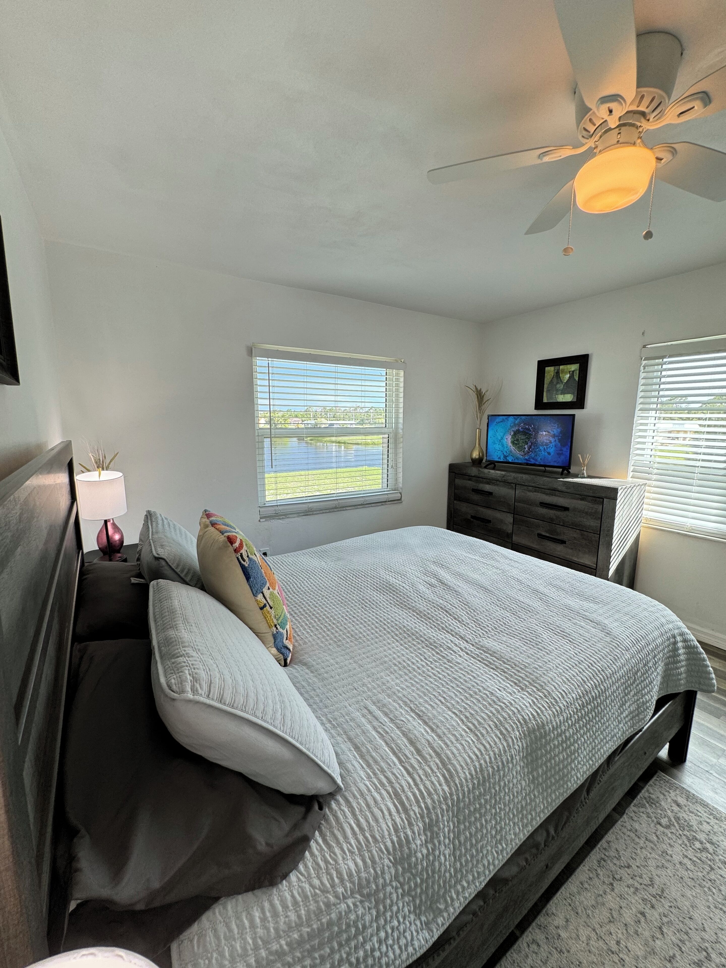 Ein Schlafzimmer mit Bett, Nachttisch, Fernseher und Deckenventilator.