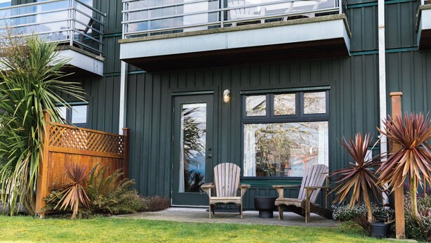 A modern building with a dark exterior, a wooden fence, and a well-maintained lawn. - Goodview Suite - licensed waterfront studio with a fireplace and patio (Tofino)
