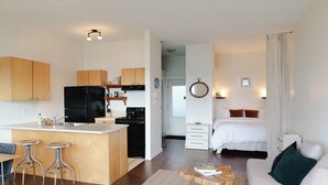 A modern kitchen with wooden cabinets, a black refrigerator, and a central island with stools. - Goodview Suite - licensed waterfront studio with a fireplace and patio (Tofino)
