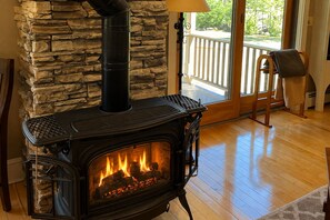 A wood-burning stove with a stone wall backdrop, a wooden chair, and a view of the outdoors through a glass door. - Ski House on quiet road - walking to Restaurants/Shops/Market...mins to Ski/Golf (Killington)