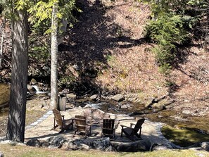 A campsite with a wooden table and four chairs, surrounded by rocks and a small stream. - Ski House on quiet road - walking to Restaurants/Shops/Market...mins to Ski/Golf (Killington)
