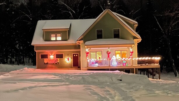 Ein zweistöckiges Haus mit schneebedecktem Dach und einer mit Lichtern geschmückten Veranda.