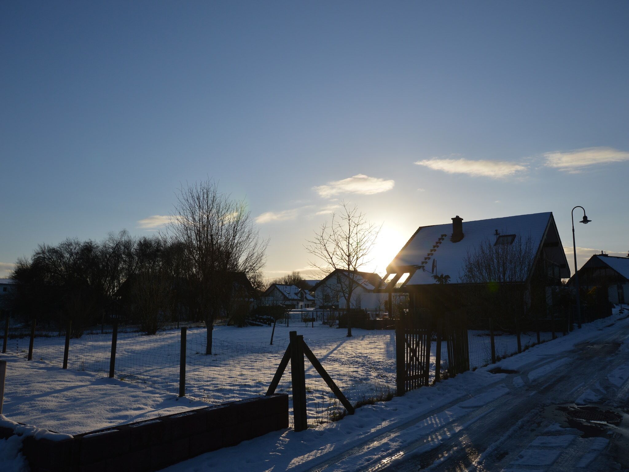 A rural landscape with a house, a wooden fence, and a snow-covered ground.