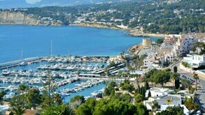 Un port de plaisance situé sur la côte, avec des bateaux, une tour historique et une ville où l’on trouve des bâtiments et de la verdure.