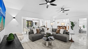 A modern living room with a grey sectional sofa, a coffee table, and two ceiling fans. - Aqua Haven- Stylish Getaway With Pool and Jacuzzi (Hollywood)