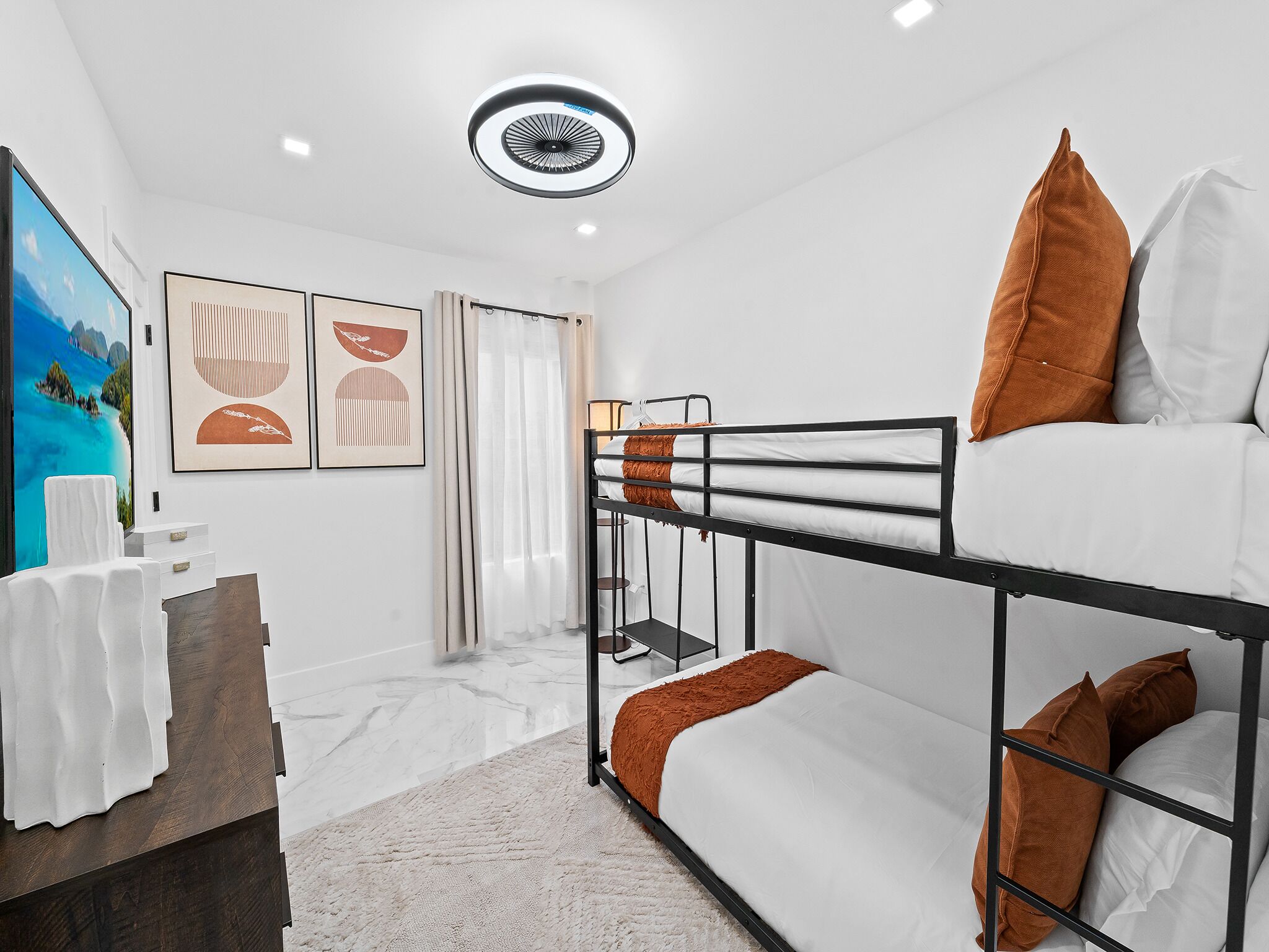 Una habitación moderna y bien iluminada con literas, un escritorio pequeño y un cuadro de una playa.