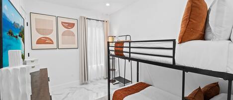 Una habitación moderna y bien iluminada con literas, un escritorio pequeño y un cuadro de una playa.
