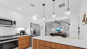 A modern kitchen with a central island, stainless steel appliances, wooden cabinetry, and pendant lighting. - Aqua Haven- Stylish Getaway With Pool and Jacuzzi (Hollywood)