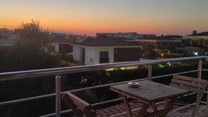 A balcony with a table and chairs, overlooking a residential area during sunset. - Otuz5 Otel (Cesme)