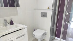A bathroom with a white sink, a purple soap dispenser, a toilet, and a glass shower enclosure. - Otuz5 Otel (Cesme)