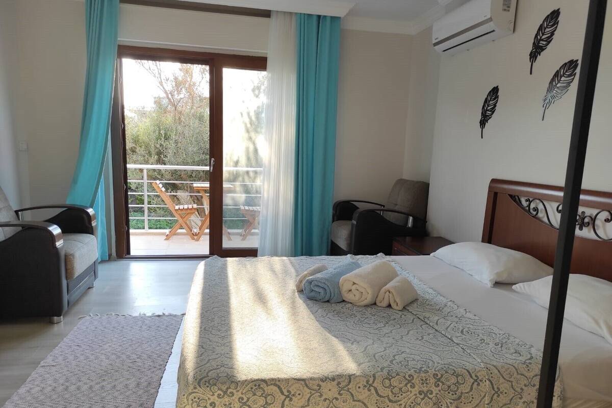 A hotel room with a bed, two chairs, a table, and a balcony with a view.