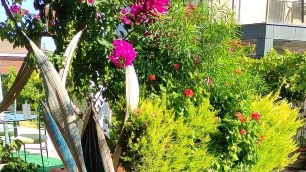 An outdoor dining area with a table set for a meal, surrounded by greenery and flowers. - Otuz5 Otel (Cesme)