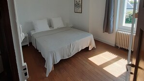 A bedroom with a bed, a nightstand, a window with curtains, and a radiator. - Seaside house 6 pers. Trébeurden pink granite coast Brittany (Trébeurden)