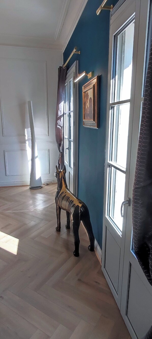A room with a wooden floor, a zebra statue, a framed picture on the wall, and a window with curtains.