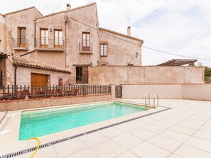Un edificio de dos pisos con piscina, mobiliario exterior y patio con baldosas.