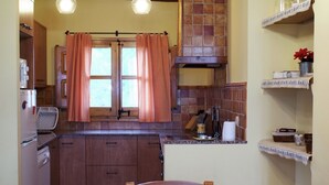 Eine kleine Küche mit Holzausbau, einem Esstisch mit Stühlen und einem Fenster mit karierten Vorhängen.