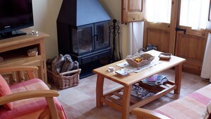 Ein gemütliches Wohnzimmer mit Fernseher, Kamin, Holzmöbeln und einem Holzkorb.