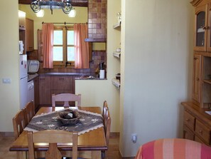 A compact kitchen with wooden cabinets, a dining table with chairs, and a window with curtains. - Cottage in Maians with Pool and Garden (Maians - Castellfollit del Boix)