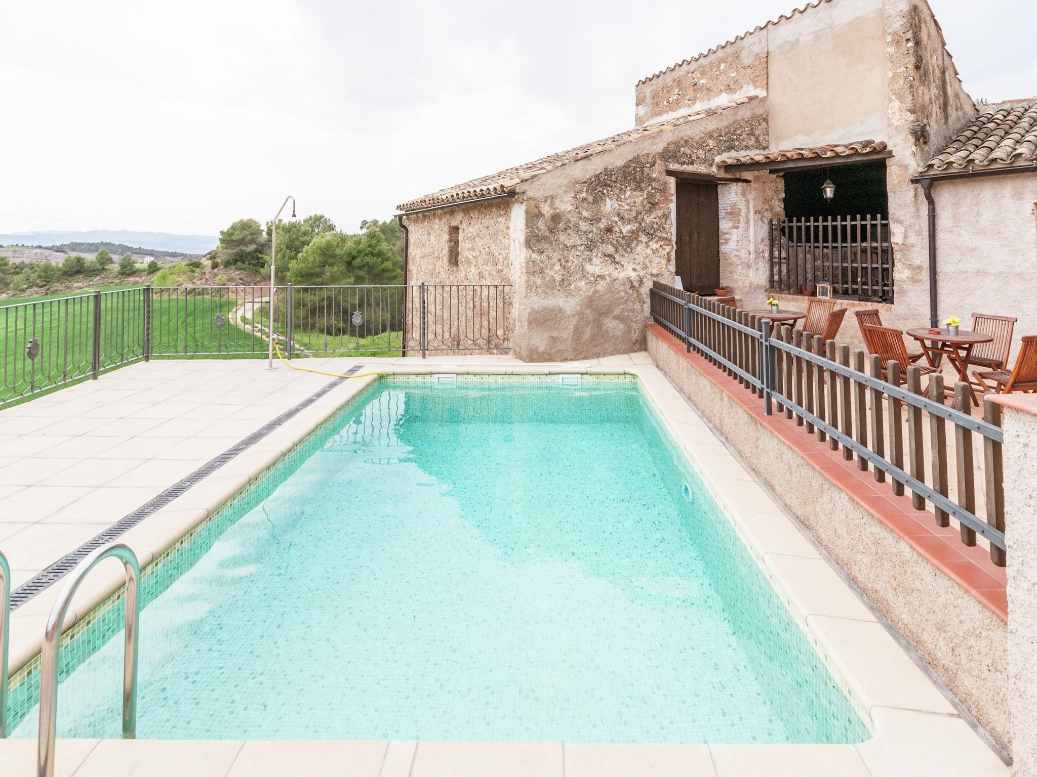 Ein Pool mit Fliesen, umgeben von einem Holzzaun und Sitzgelegenheiten im Freien.