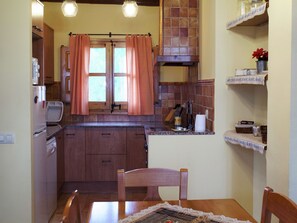 Una cocina compacta con armarios de madera, una mesa de comedor con sillas y una ventana con cortinas a cuadros.