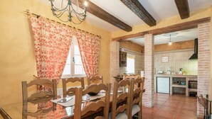 Un comedor con una mesa y sillas de madera, una araña y vista a la cocina.