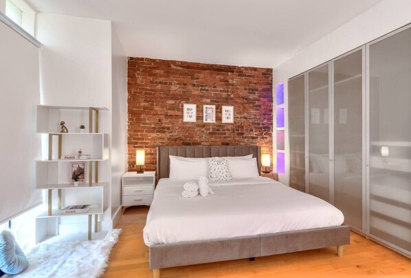A modern bedroom with a brick wall, a large bed, white shelving, and a wardrobe. - Take a break in a modern loft on the plateau (Montréal)