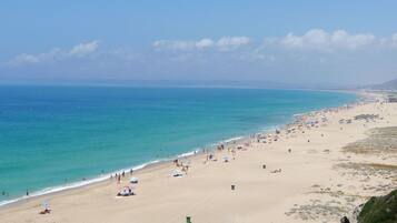Een breed strand met helderblauw water, parasols en mensen.
