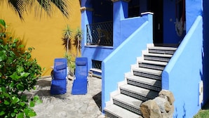 Un bâtiment aux murs extérieurs bleus et jaunes, un escalier menant à une porte, et deux fauteuils bleus.
