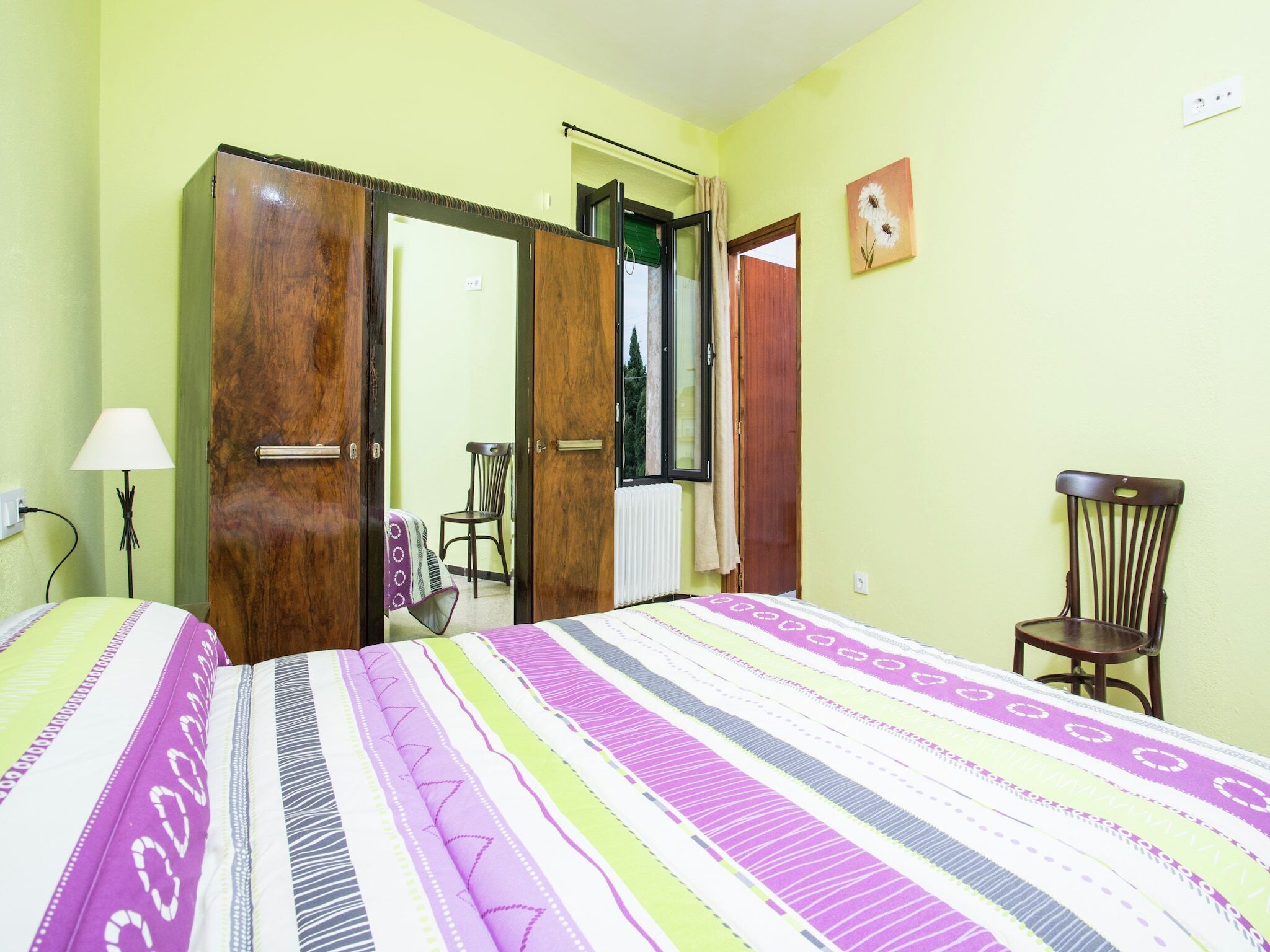 A room with a bed, a wooden wardrobe, a chair, and a window.
