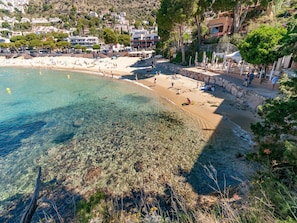 A beach with clear water, a stone wall, and buildings in the background. - Holiday Home in St Pere Pescador with Pool (Sant Pere Pescador)