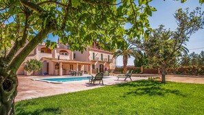 Una villa con piscina, mobiliario exterior y un jardín exuberante.