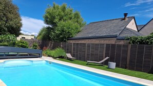 Une piscine avec une terrasse carrelée, une chaise longue et une clôture en bois.
