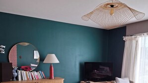 Un salon moderne avec un mur d’accent de couleur turquoise, un miroir rond, une bibliothèque, un téléviseur et des sièges confortables.