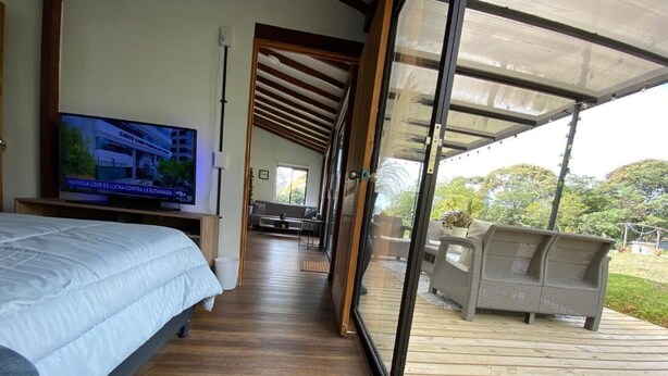 Quarto com cama, televisão e vista para o exterior através de uma porta de vidro.