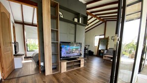 Ampla sala de estar com uma grande televisão de tela plana, piso de madeira e vista para um deck externo através de uma porta de vidro.