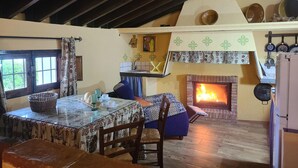 Un interior rústico con comedor, chimenea y cocina con ollas colgantes.