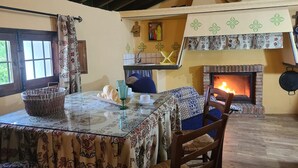 Un comedor acogedor con chimenea, una mesa dispuesta con platos y una cesta, y vista a la cocina.