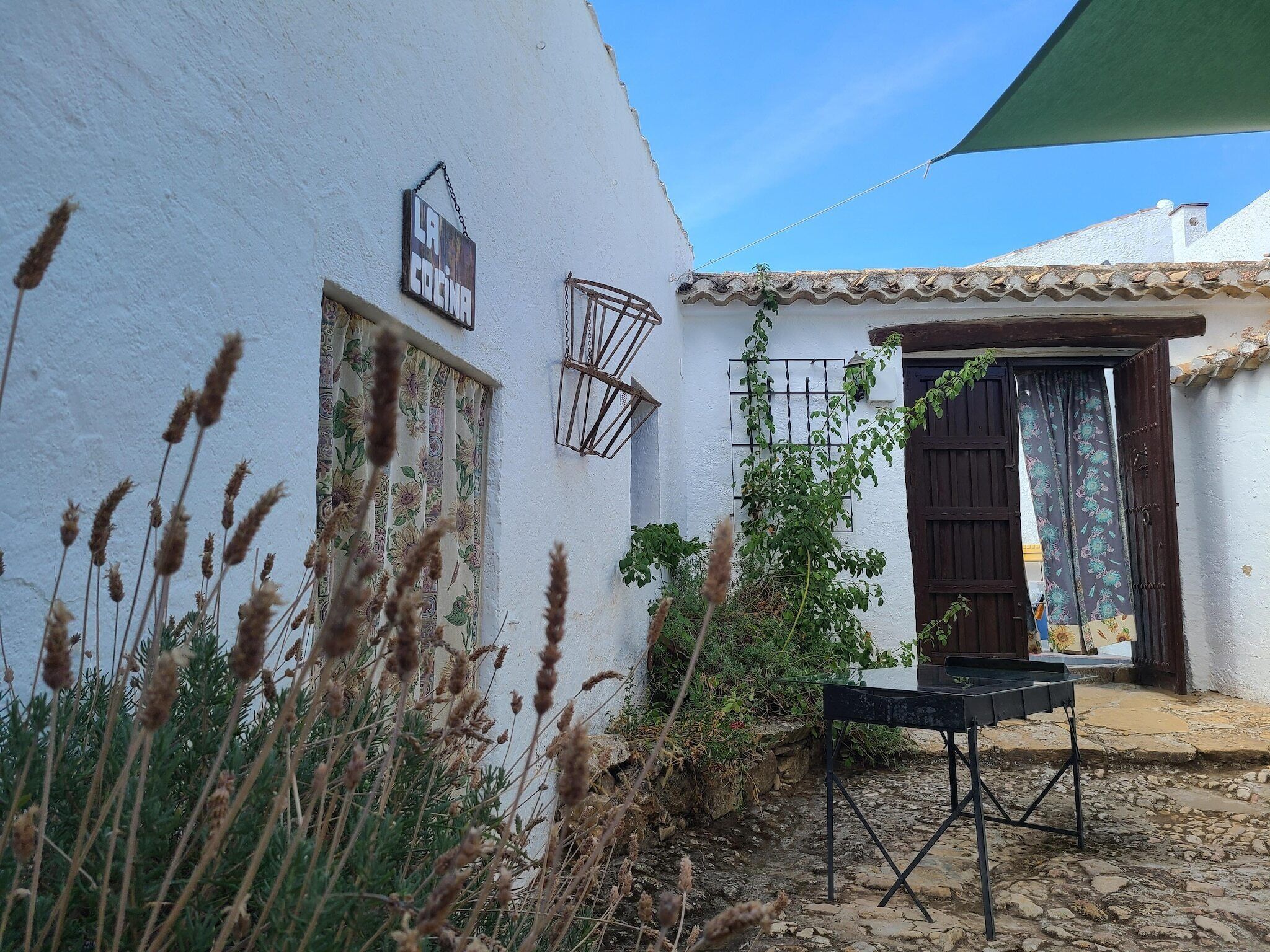 A white building with a sign reading 'LA COCINA,' a metal gate, and a table with a chair outside.