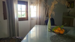 Un comedor con una mesa, un jarrón con plantas secas y un frutero.